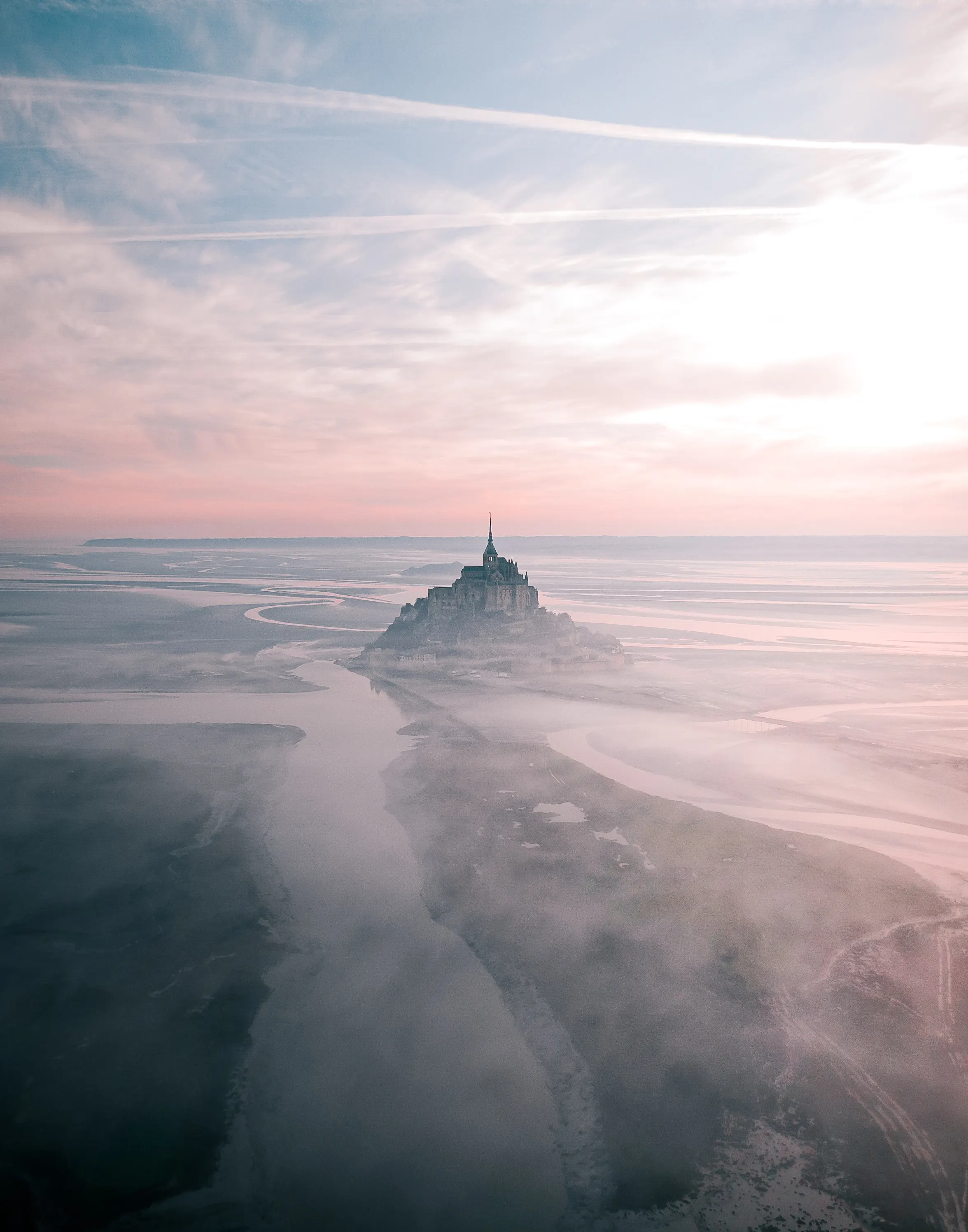 Mont Saint-Michel at low tide with tidal streams across the sand
